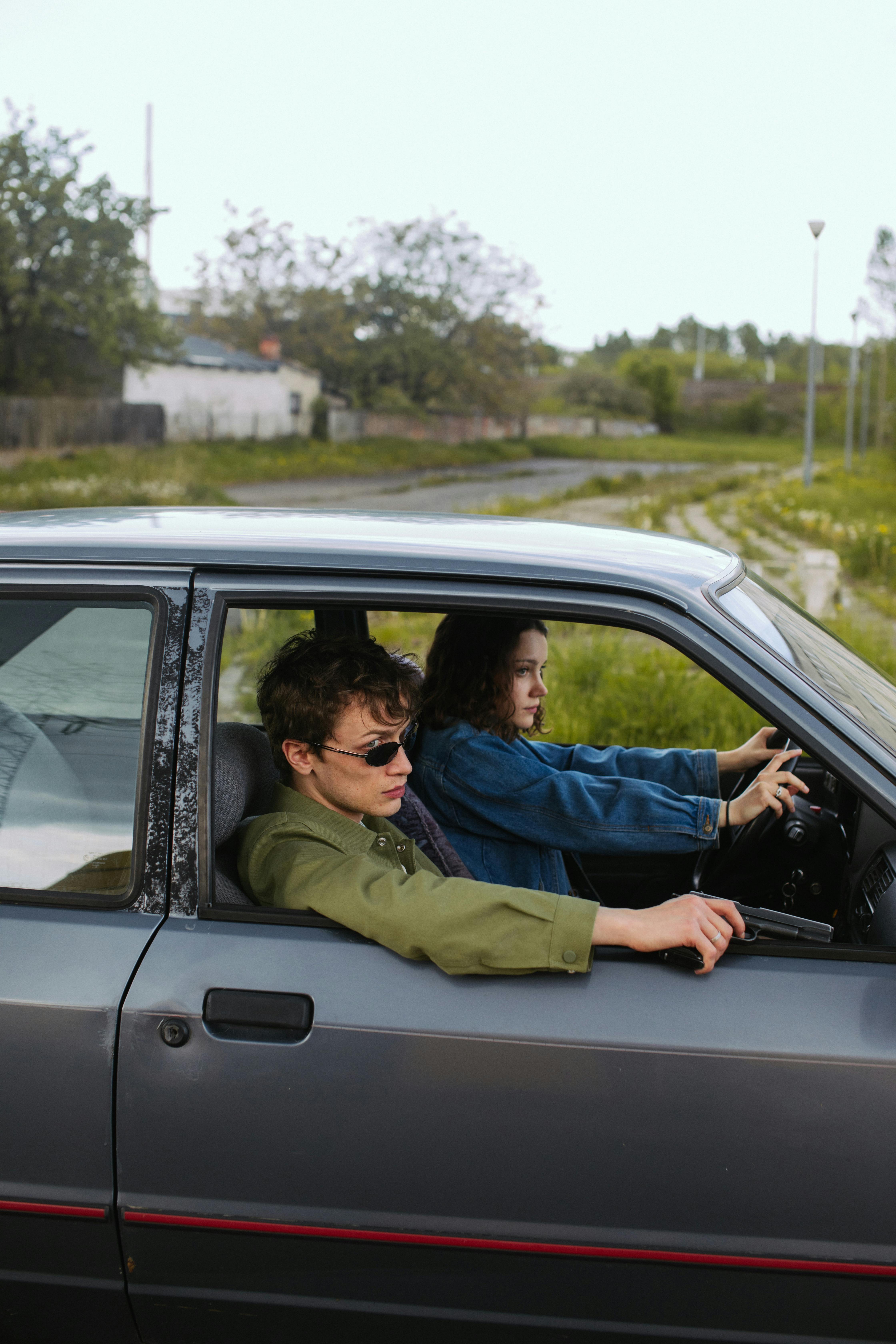 A young couple in an old car, holding guns. Dramatic and intense scene.