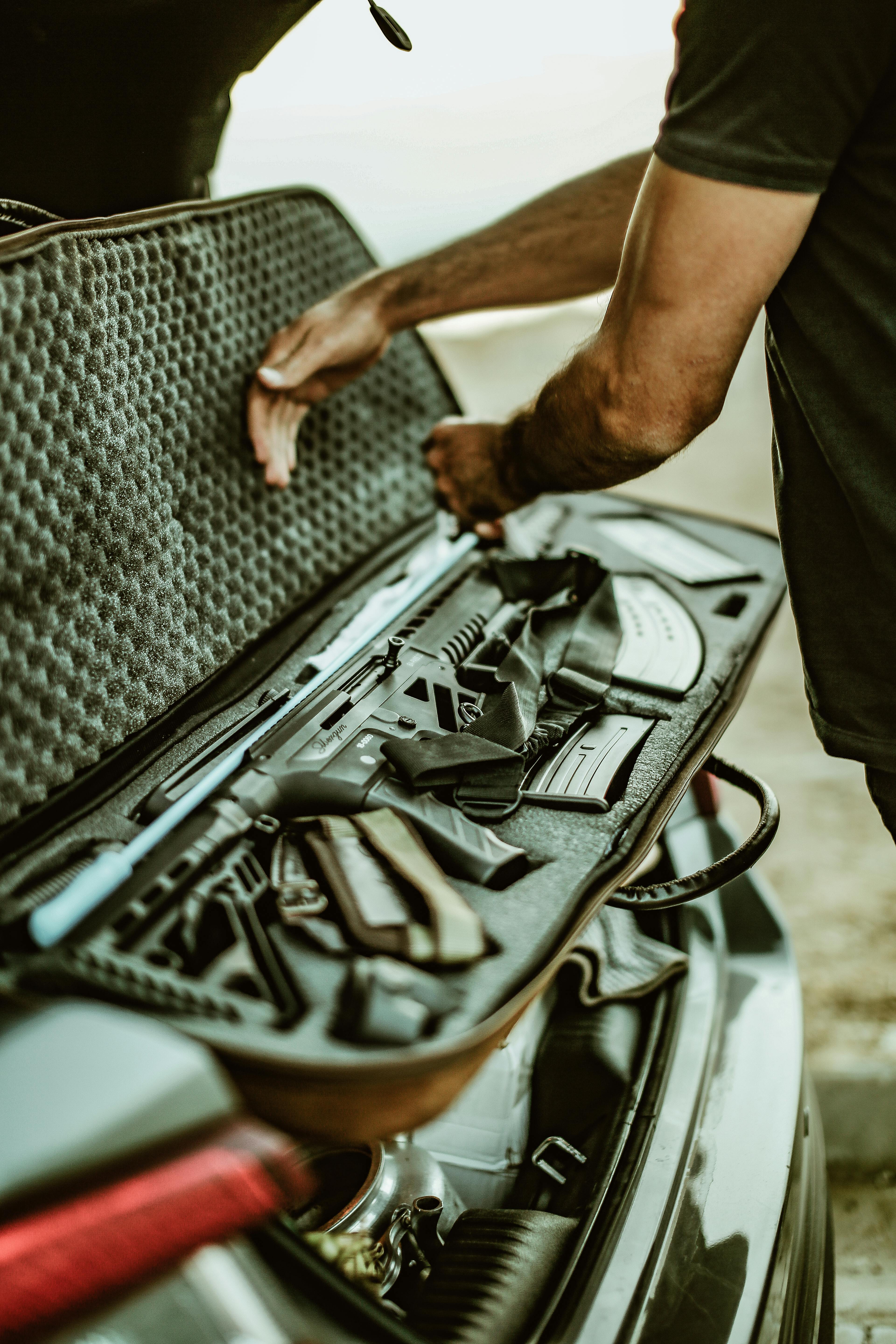 A man opens a rifle case in the trunk of a car, showcasing firearms and accessories.