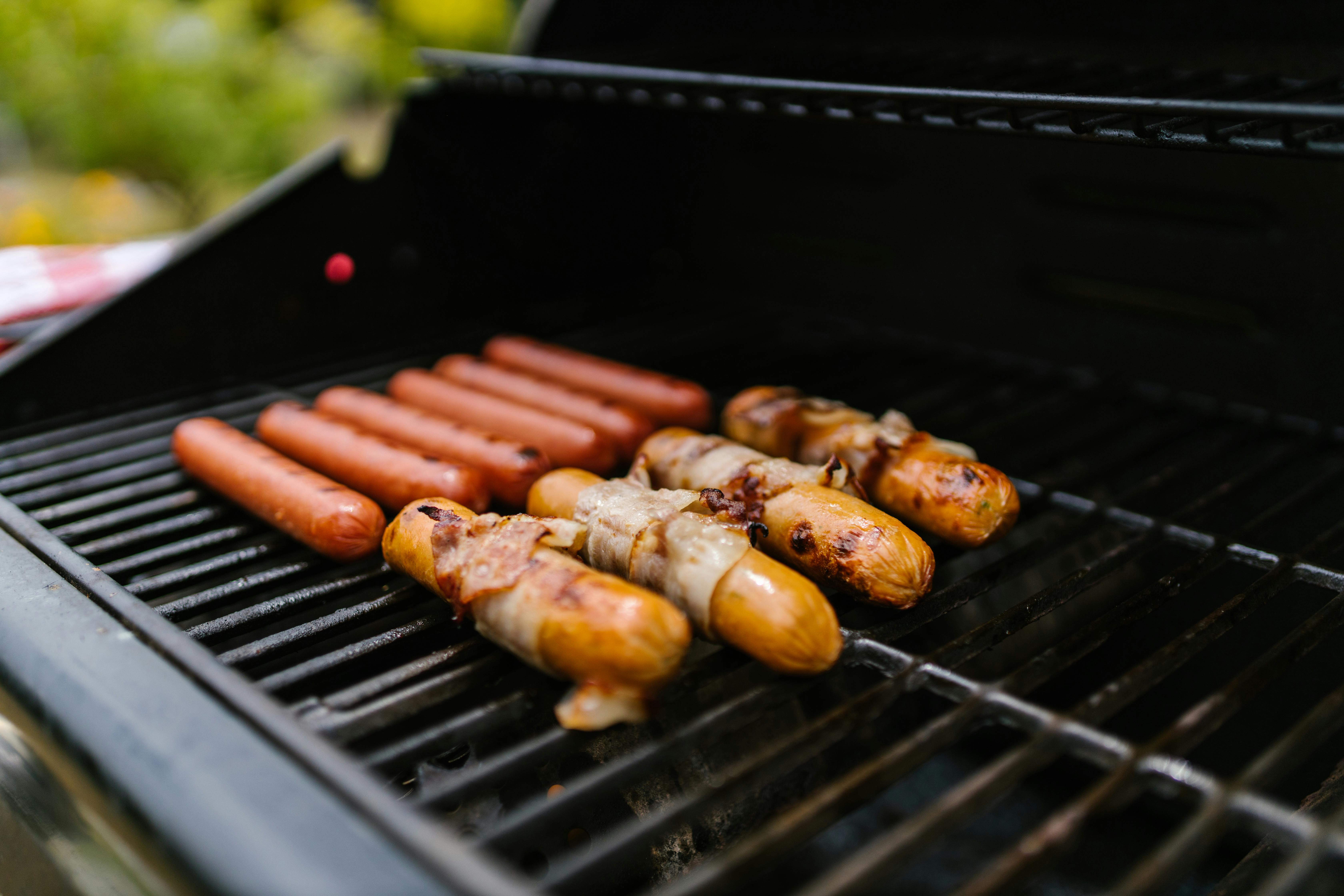 Close-up of hotdogs and bacon-wrapped sausages on a grill outdoors.